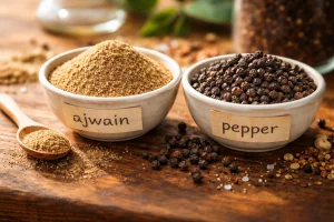 Ajwain powder and black pepper in labeled spice bowls under warm light